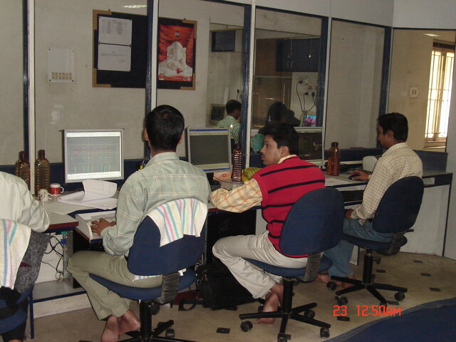 Four employees working at computer desks in an office environment with monitors and documents.